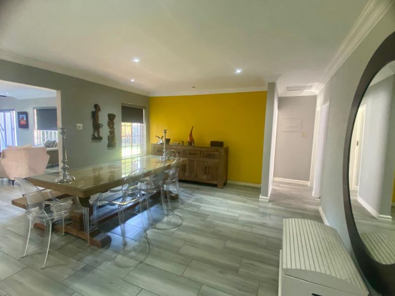 A bright dining area featuring modern tiled flooring, recessed downlighting, and a bold yellow accent wall, creating a functional and inviting space.