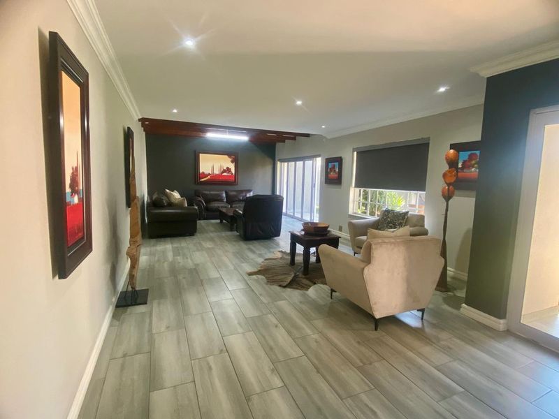Spacious living room featuring modern wood-look tiled flooring, recessed downlighting, decorative timber ceiling beams, and large sliding glass doors leading to the exterior.