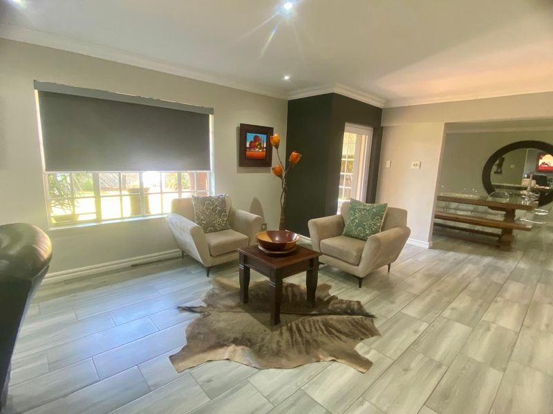A bright living room featuring modern wood-look tiled flooring, recessed downlights, and large windows with roller blinds.
