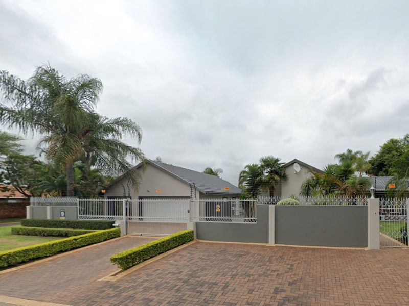 Front view of the property featuring a paved driveway, secure perimeter wall with electric fencing, and a private garage entrance.