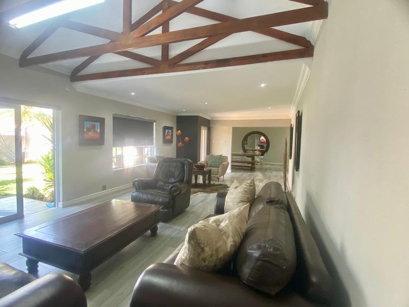 Spacious open-plan living area featuring exposed timber roof trusses, modern laminate flooring, and large sliding glass doors providing access to the garden.