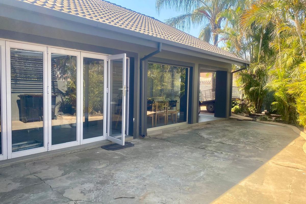 Rear exterior view of the house featuring a concrete patio, bi-fold glass doors, and large windows under a tiled roof.