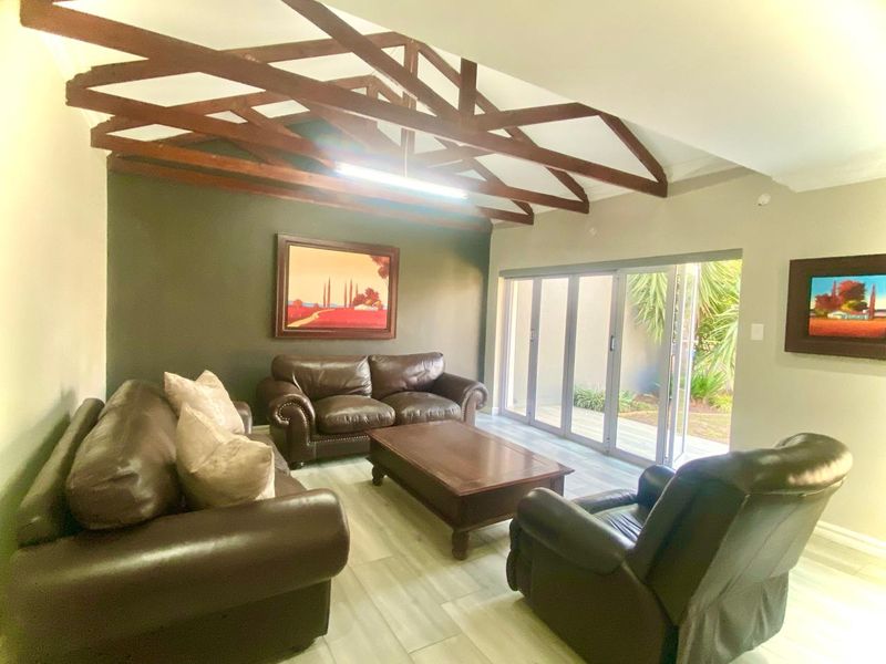 Spacious living room featuring exposed timber ceiling beams, modern laminate flooring, and large aluminium stacker doors providing seamless access to the outdoor area.