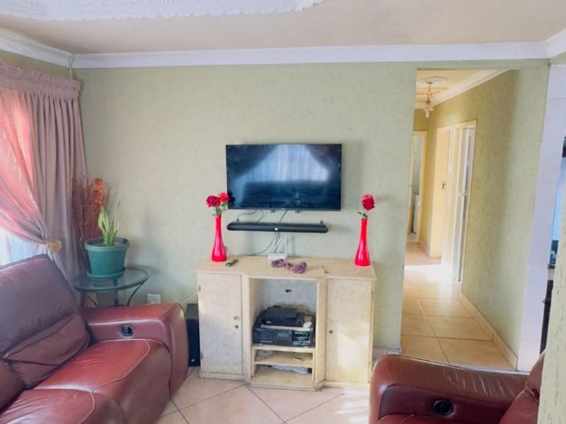 A living room featuring ceramic floor tiles, decorative ceiling cornices, and a central ceiling rose, providing a functional and lived-in space.