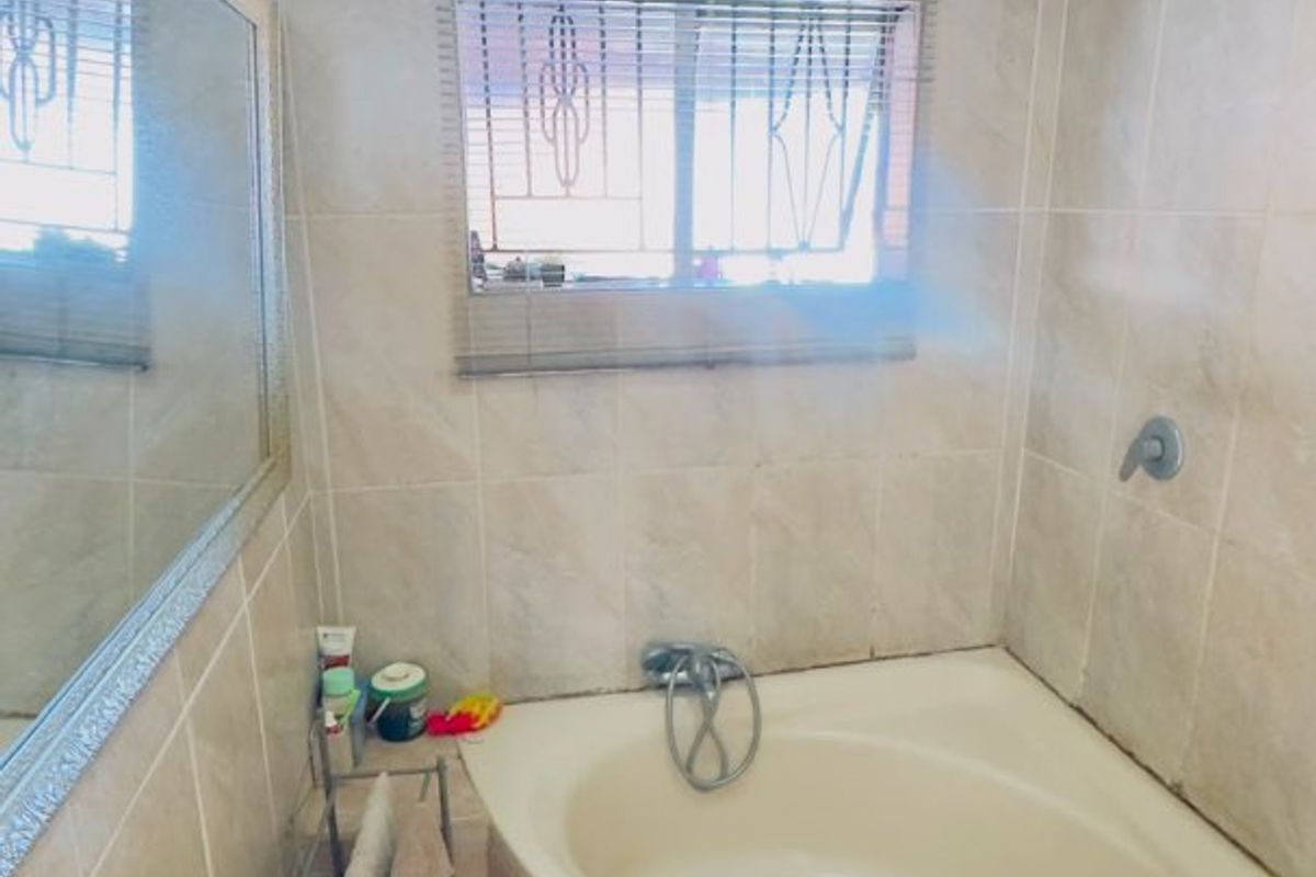 A functional bathroom featuring a corner bathtub, wall-mounted shower, and tiled finishes, offering a practical layout with potential for modern updates.