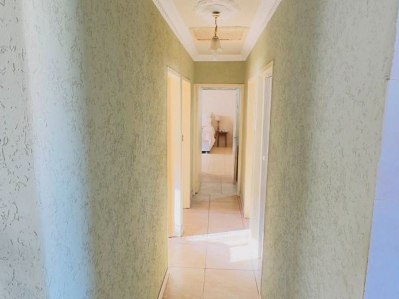 A functional hallway featuring tiled flooring, textured wall finishes, and decorative ceiling cornicing, providing access to adjacent rooms.