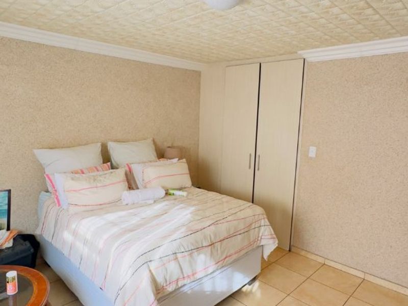 A bedroom featuring tiled flooring, textured ceiling tiles, and built-in cupboards, offering a functional space with neutral finishes.