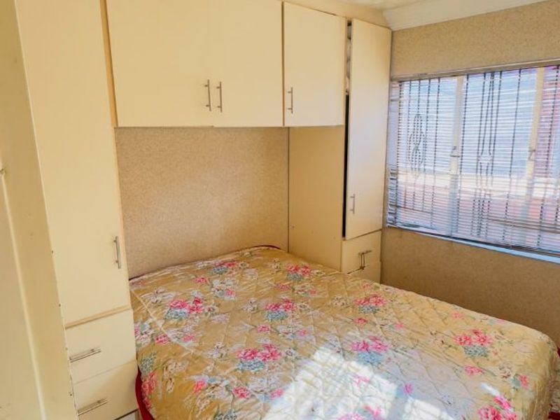 A compact bedroom featuring built-in cupboards, tiled flooring, and a textured ceiling, offering a functional space with potential for modern updates.