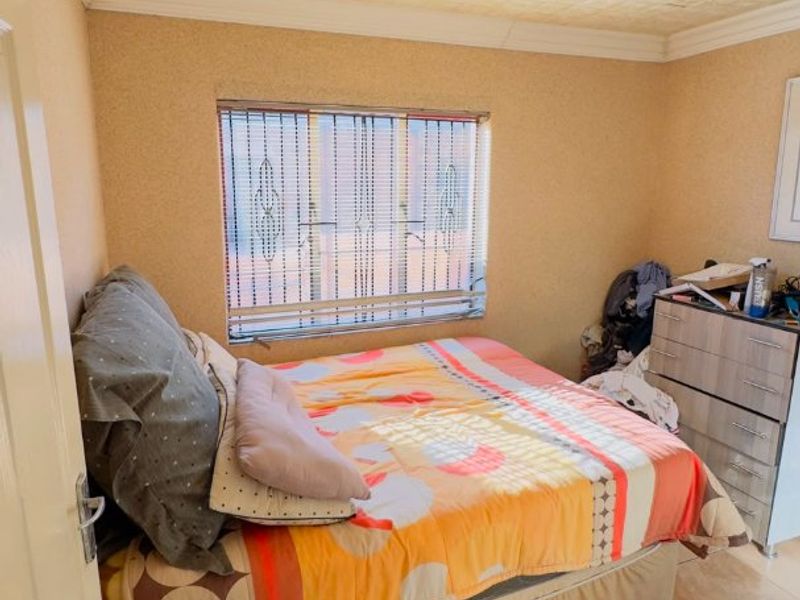 A bedroom featuring tiled flooring, textured ceiling tiles, and a window with security bars, offering a functional space in need of cosmetic updates.
