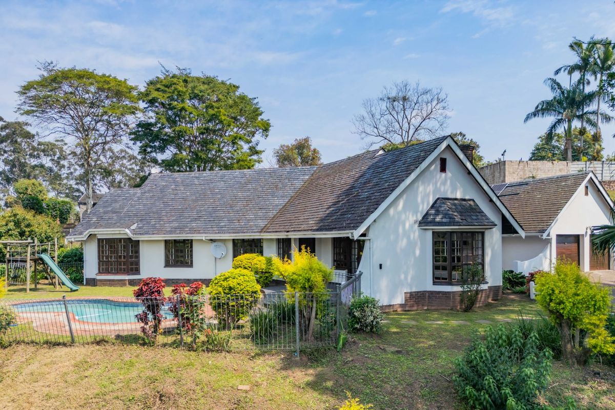 Rear view of the house featuring a swimming pool, landscaped garden, and a tiled roof with a prominent bay window.