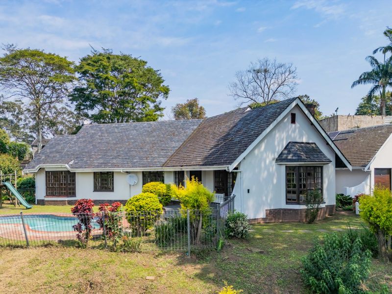 Rear view of the house featuring a swimming pool, landscaped garden, and a tiled roof with a prominent bay window.