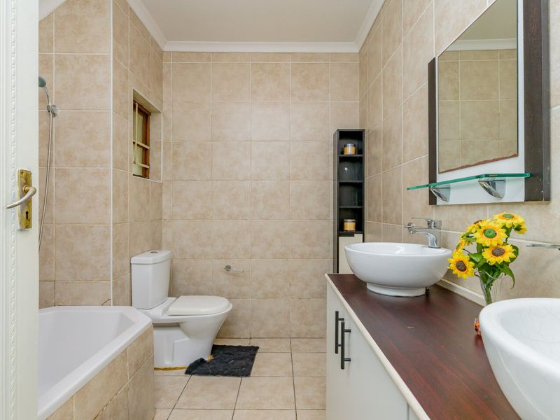 A functional bathroom featuring a bathtub, toilet, and a double vanity with vessel sinks, finished with neutral wall and floor tiling.