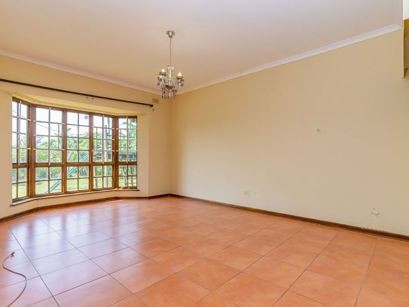 A spacious, empty living room featuring large bay windows, ceramic tile flooring, and a classic chandelier, offering a blank canvas for interior design.