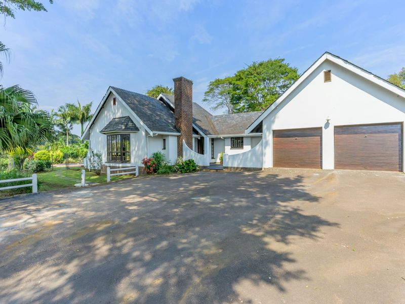 Front elevation of a single-story residence featuring a double garage, brick chimney, and an asphalt driveway set within a landscaped garden.