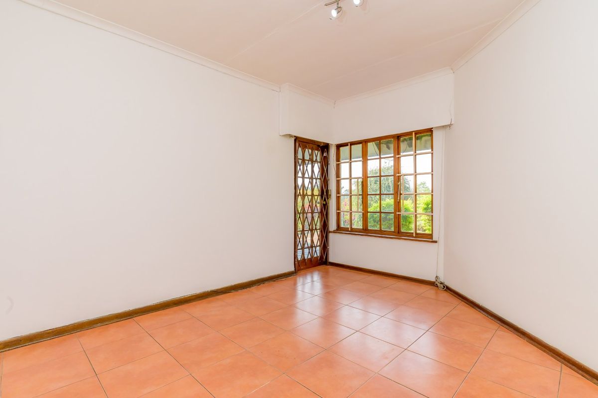 An empty bedroom featuring ceramic tile flooring, wooden window frames, and a security gate, offering a blank canvas for personalization.