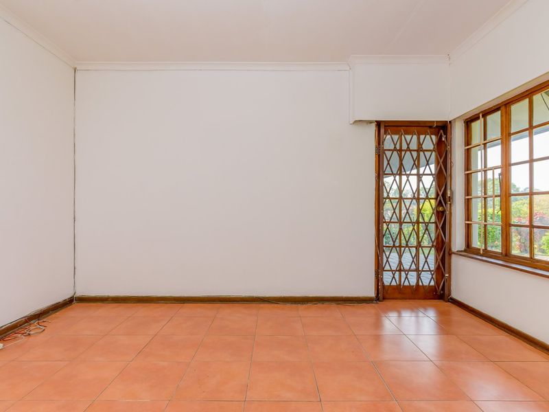 An empty living room featuring ceramic tile flooring, wooden window frames, and a security gate leading to the exterior.