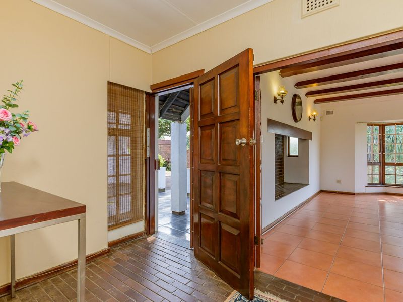 Welcoming entrance hall featuring exposed timber ceiling beams, brick flooring, and a seamless transition into the adjacent living area with a built-in fireplace.