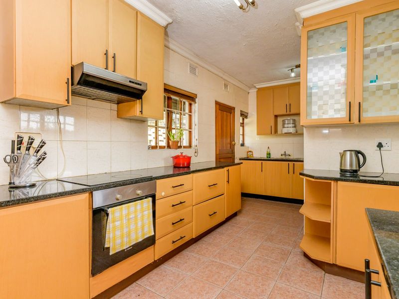A functional kitchen featuring light wood cabinetry, granite countertops, built-in oven and hob, and tiled flooring throughout.
