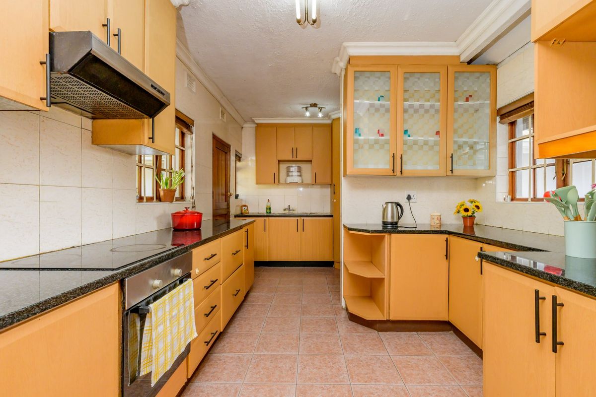 A functional kitchen featuring light wood cabinetry, granite countertops, a built-in oven and hob, and tiled flooring with a classic layout.