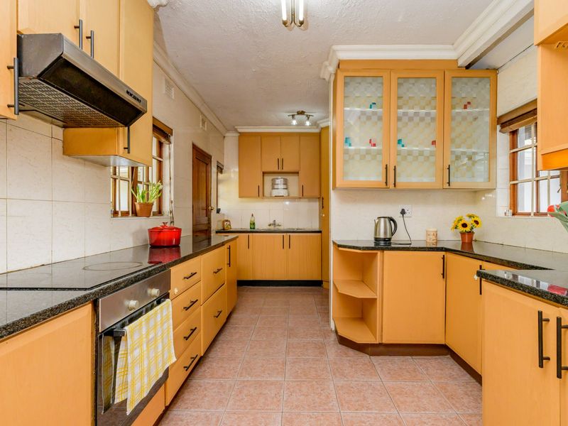 A functional kitchen featuring light wood cabinetry, granite countertops, a built-in oven and hob, and tiled flooring with a classic layout.