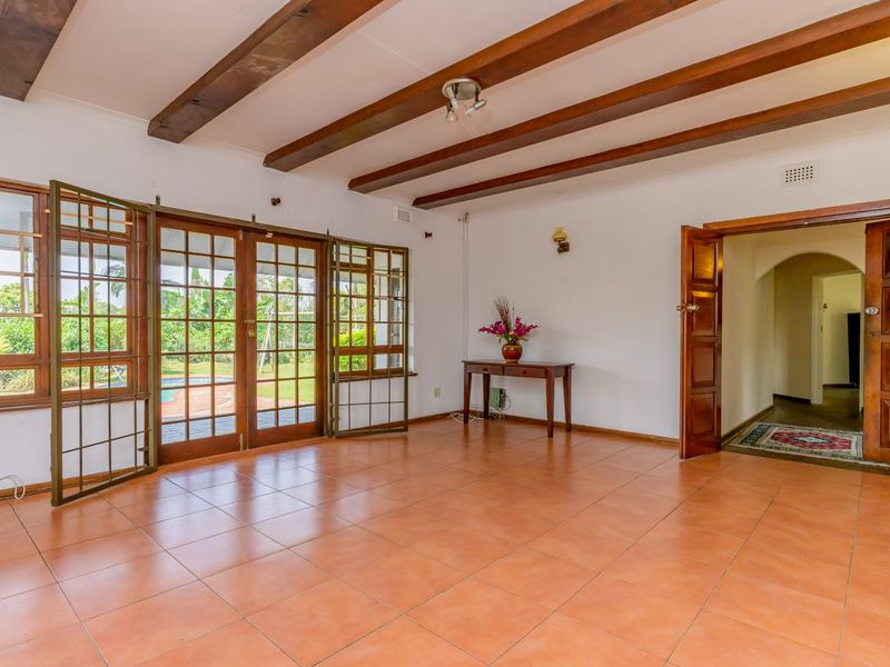Spacious living area featuring exposed timber ceiling beams, terracotta floor tiles, and large timber-framed glass doors providing access to the garden.