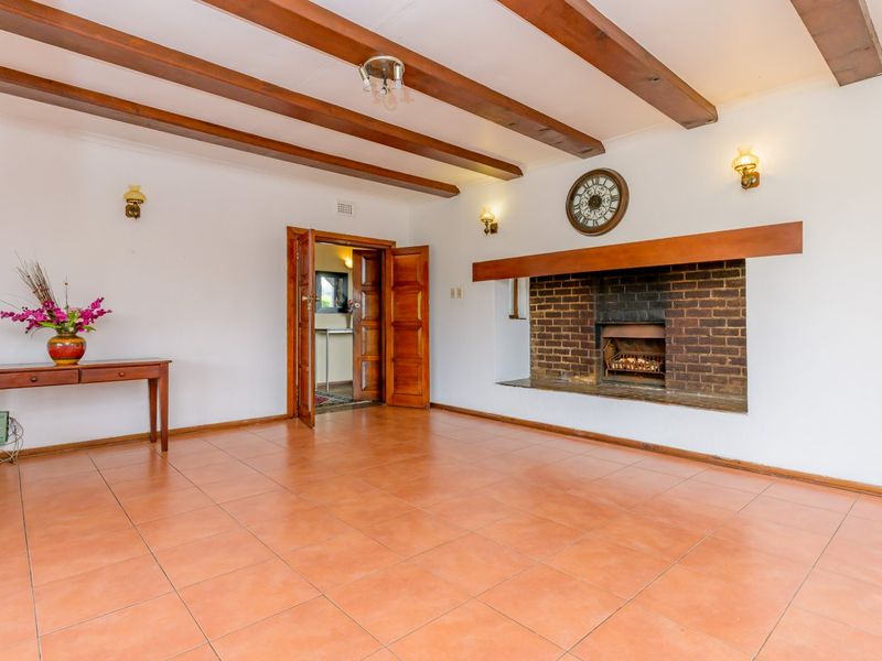 Spacious living room featuring exposed timber ceiling beams, a classic brick fireplace with a timber mantel, and durable ceramic floor tiles.