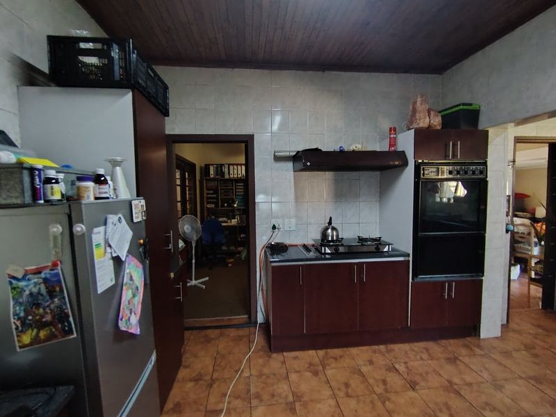 A dated kitchen featuring dark wood cabinetry, a built-in oven, gas hob, tiled backsplash, and timber ceiling, requiring modernization and electrical safety improvements.