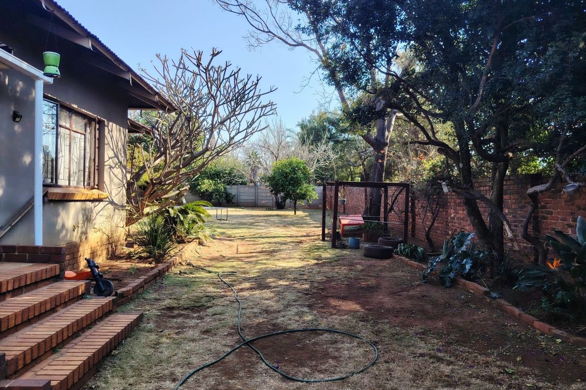 A spacious rear garden featuring a brick boundary wall, mature trees, and brick steps leading from the house.