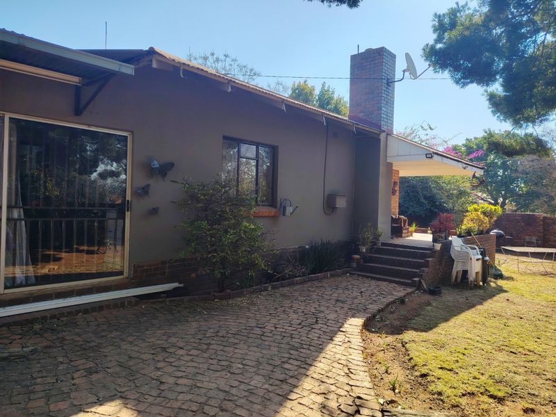 Rear view of the house featuring a brick chimney, paved walkway, and a covered patio area leading to the garden.