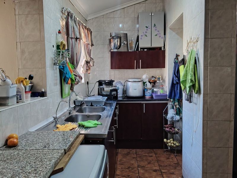 A functional scullery area featuring tiled walls, double stainless steel sink, and built-in cabinetry, providing additional prep and wash-up space.
