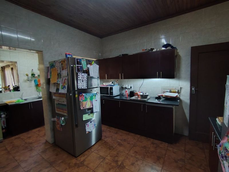 A functional kitchen featuring dark wood cabinetry, stone countertops, tiled backsplash, and a timber ceiling, with an adjacent scullery area visible.
