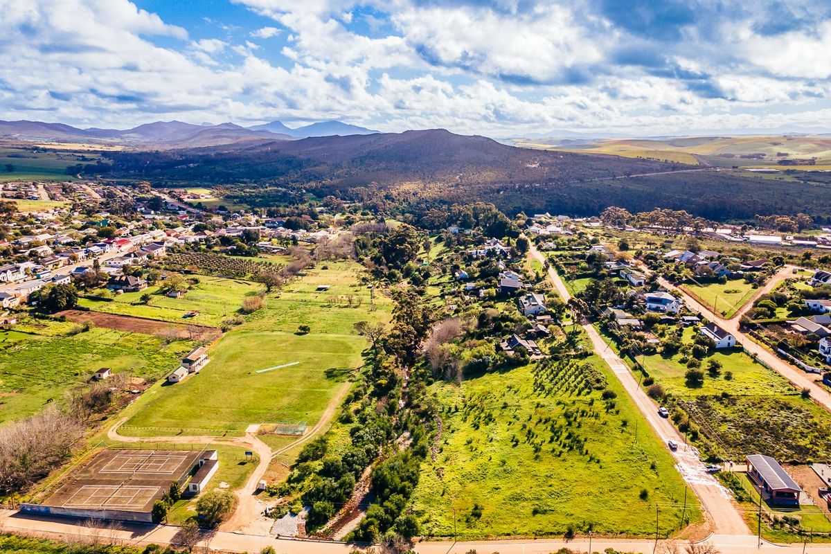 An aerial view of a residential area featuring open land, a tennis court, and surrounding natural landscape with mountain views.
