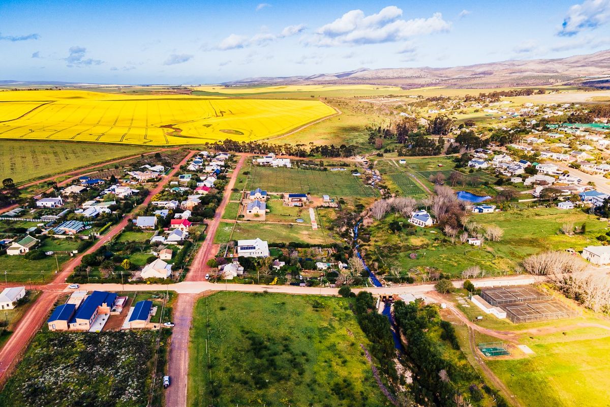 An aerial view of a residential area featuring vacant land plots, gravel road access, and surrounding agricultural fields.