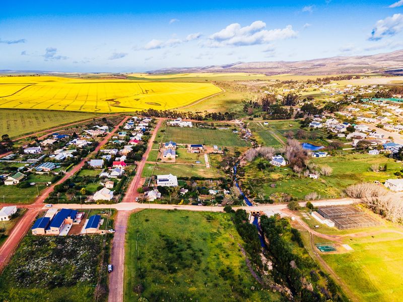 An aerial view of a residential area featuring vacant land plots, gravel road access, and surrounding agricultural fields.