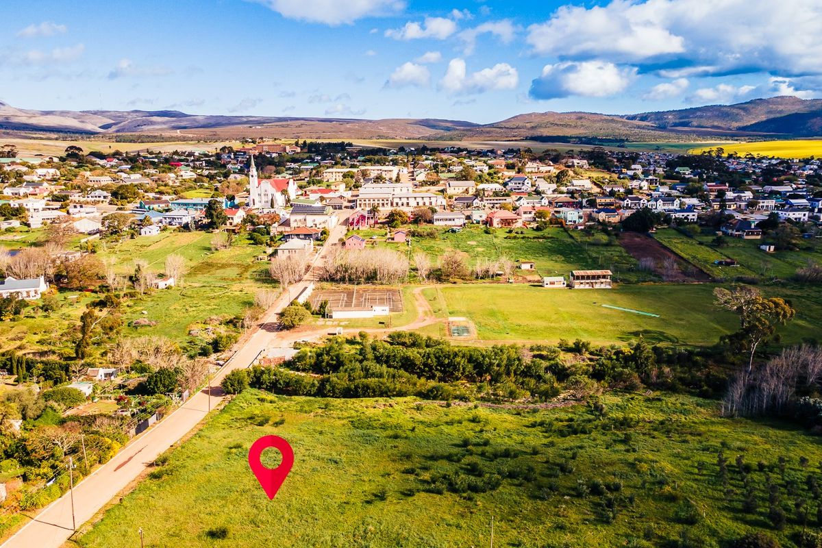 Aerial view of a vacant residential plot situated in a rural town setting with surrounding landscape and road access.