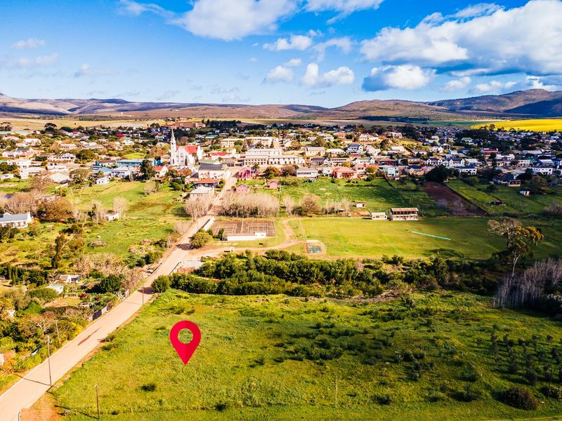 Aerial view of a vacant residential plot situated in a rural town setting with surrounding landscape and road access.