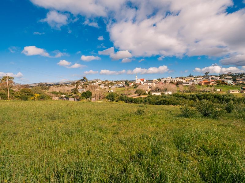 A scenic view of an open grassy field with a residential town and church visible in the background under a blue sky.