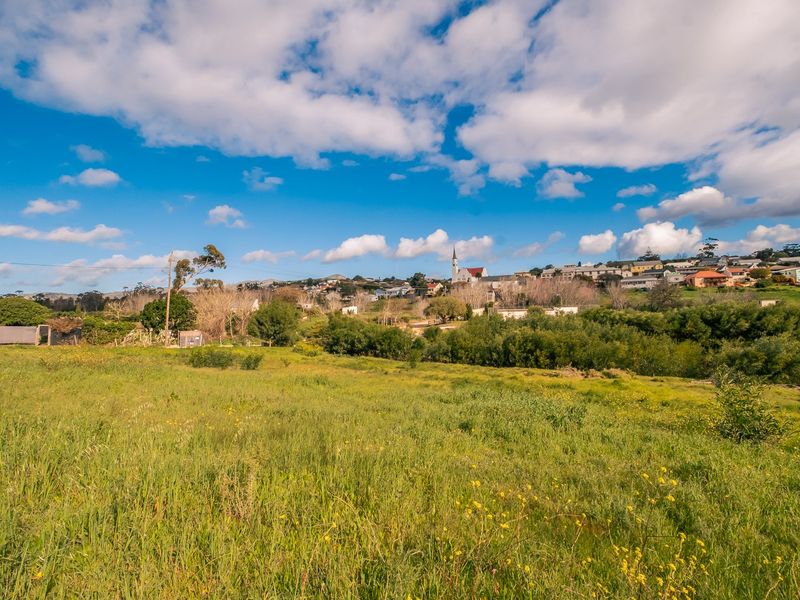A wide-angle view of a vacant residential plot featuring natural vegetation with a distant view of the surrounding town and landscape.