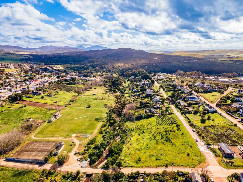 An aerial view of a residential area featuring open land, a tennis court, and surrounding natural landscape with mountain views.