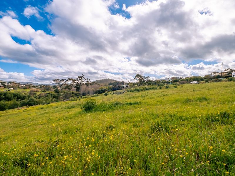 A wide-angle view of a sloped, undeveloped residential plot featuring natural grass and vegetation with distant hillside views.