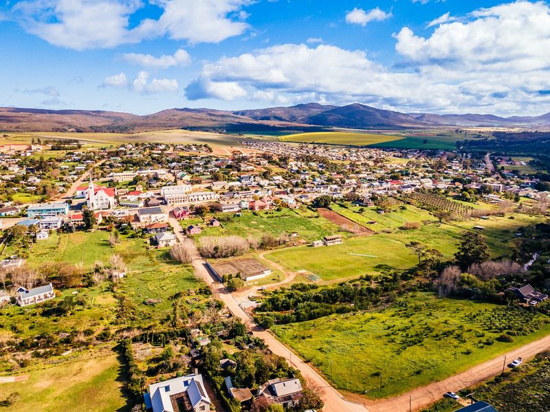 An aerial view of a residential town landscape featuring open green spaces, surrounding hills, and established neighborhood infrastructure.