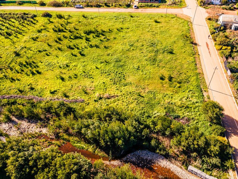 An aerial view of a vacant residential plot featuring natural grassland, road access, and a bordering creek.