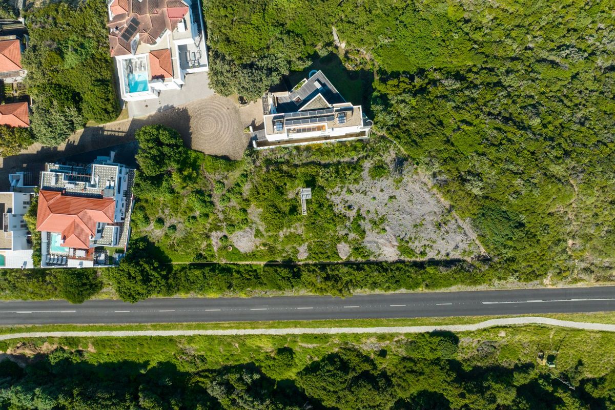 Aerial view of a residential vacant land plot situated between established properties and a road, featuring natural vegetation and surrounding residential infrastructure.