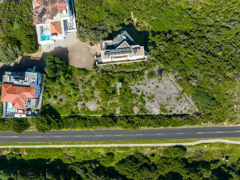 Aerial view of a residential vacant land plot situated between established properties and a road, featuring natural vegetation and surrounding residential infrastructure.