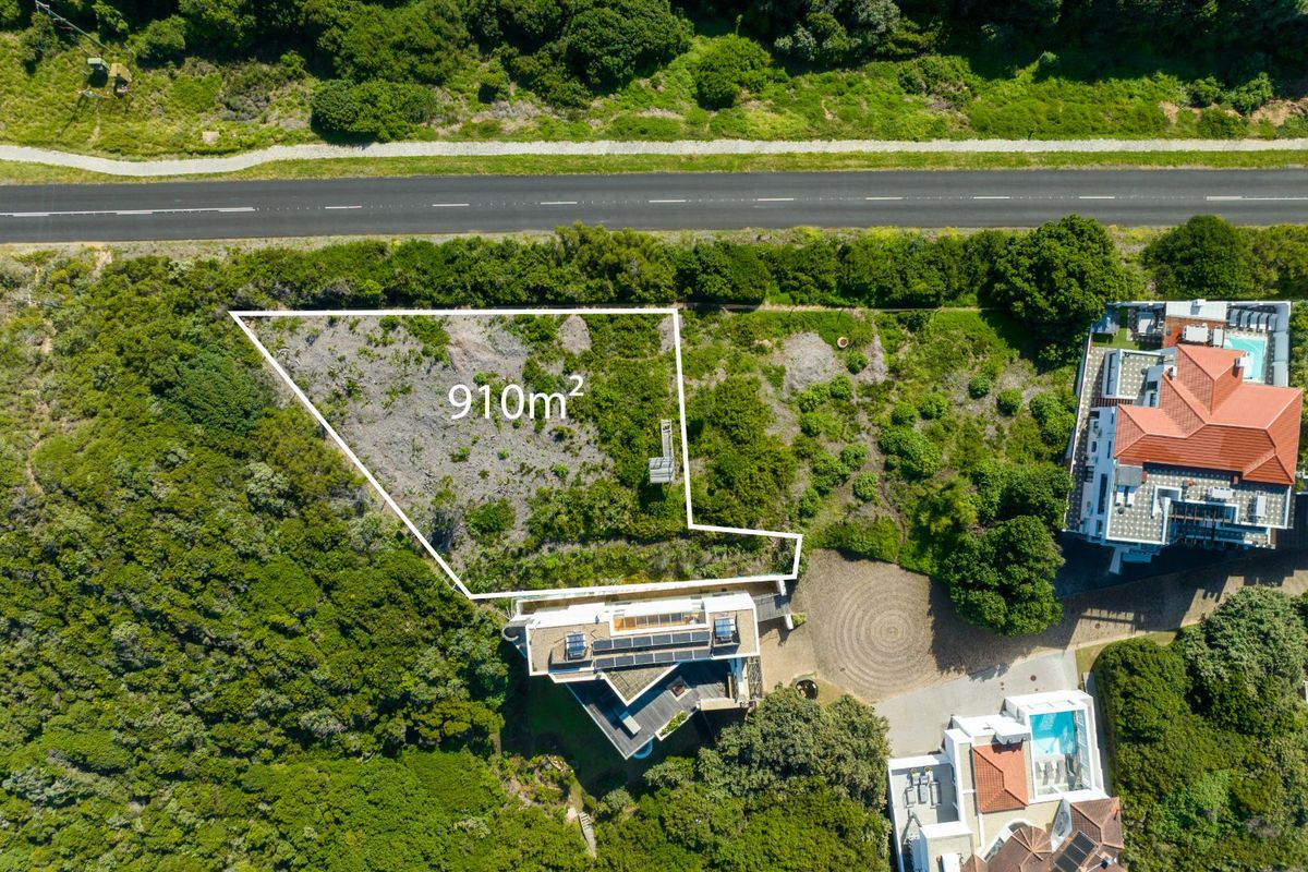 Aerial view of a 910m2 vacant residential plot situated adjacent to a road and existing residential properties.
