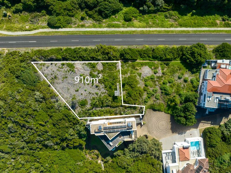 Aerial view of a 910m2 vacant residential plot situated adjacent to a road and existing residential properties.