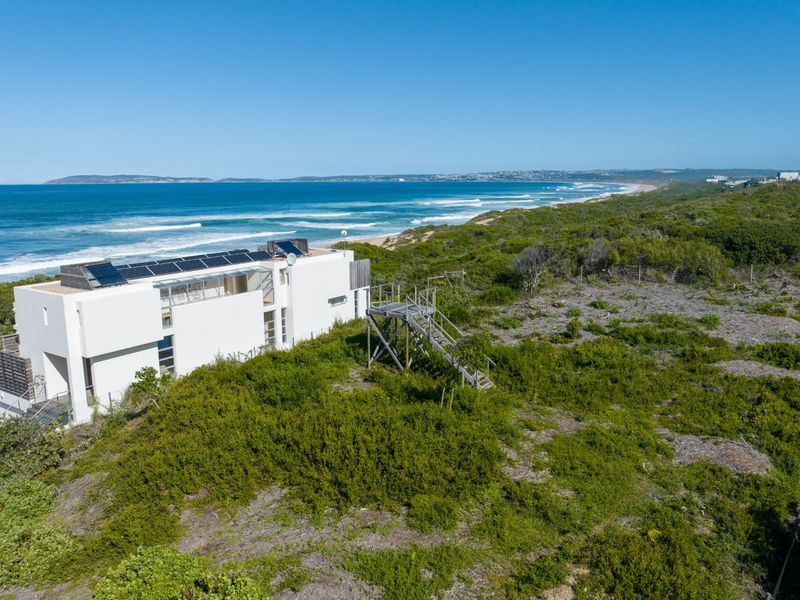 Aerial view of a modern coastal property featuring solar panels, a wooden viewing platform, and direct access to the surrounding natural landscape and beach.