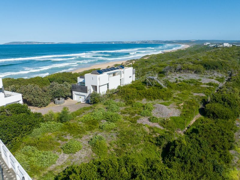 Aerial view of a coastal residential property featuring solar panels, surrounded by natural vegetation with direct proximity to the beach and ocean.