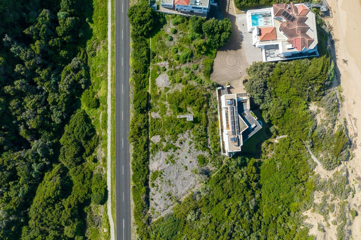 Aerial view of a vacant residential plot situated between a road and coastal vegetation, offering potential for development.