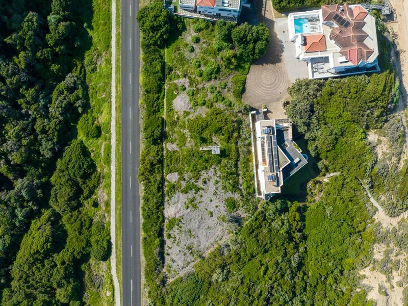 Aerial view of a vacant residential plot situated between a road and coastal vegetation, offering potential for development.
